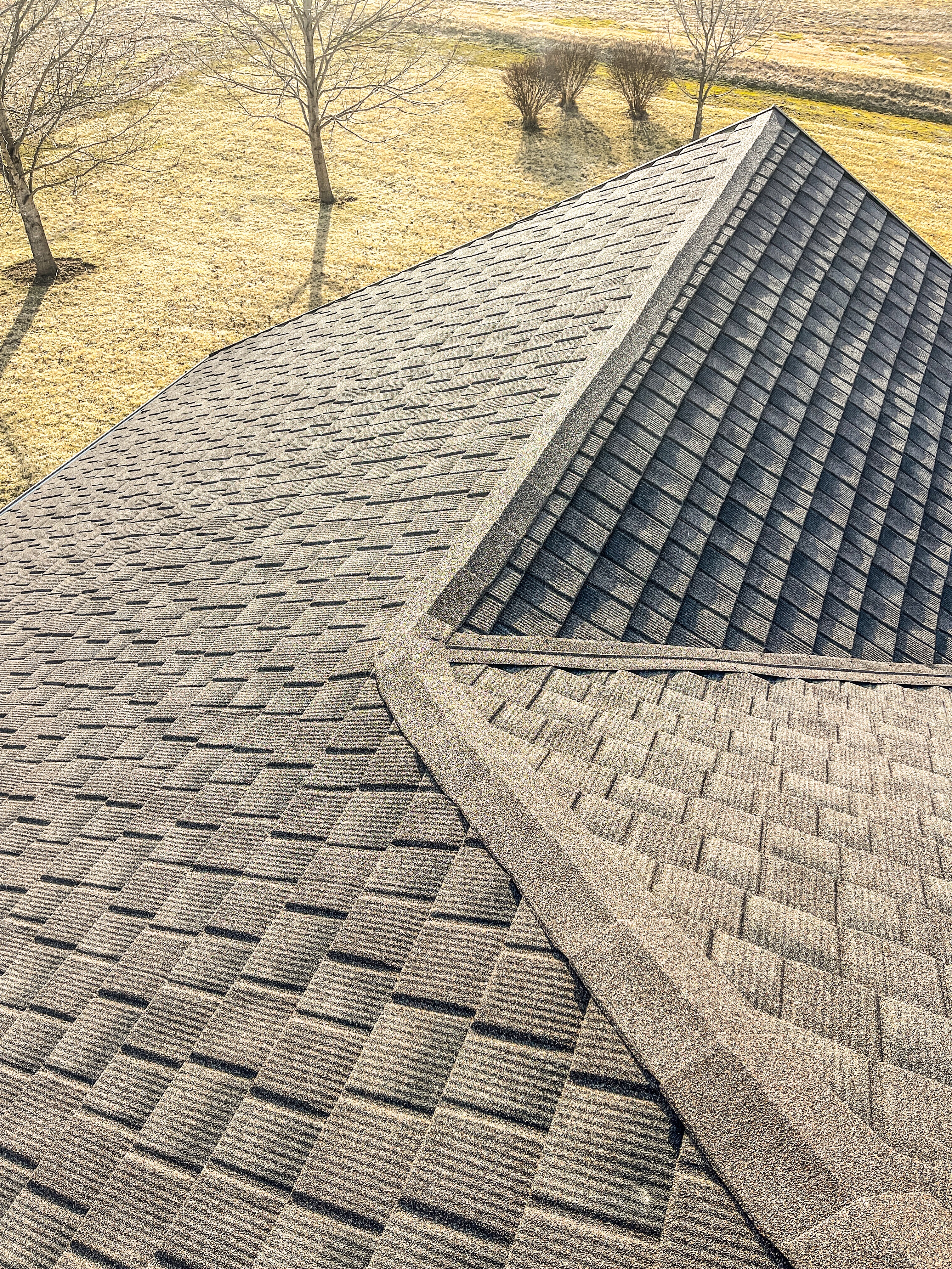 Image of a Tilcor Roof overview. You can see a new armored roof on a residential home. There are gray shingles and yellow grass down below. 